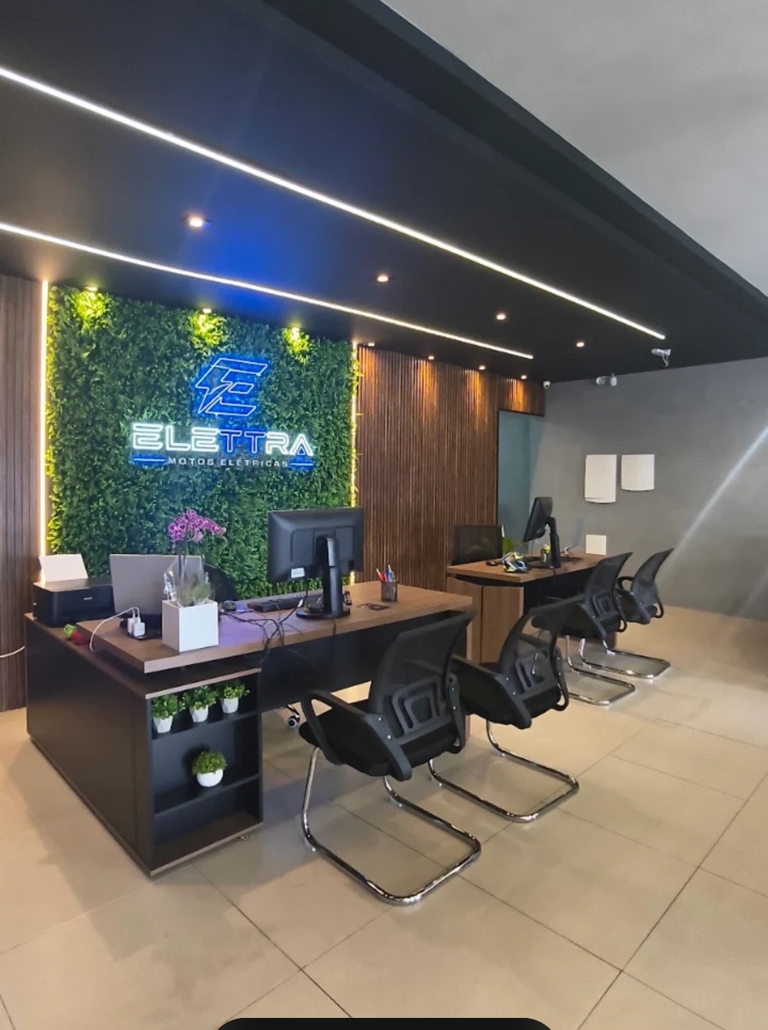 Interior do showroom Elettra com recepção moderna e jardim vertical com logo em neon